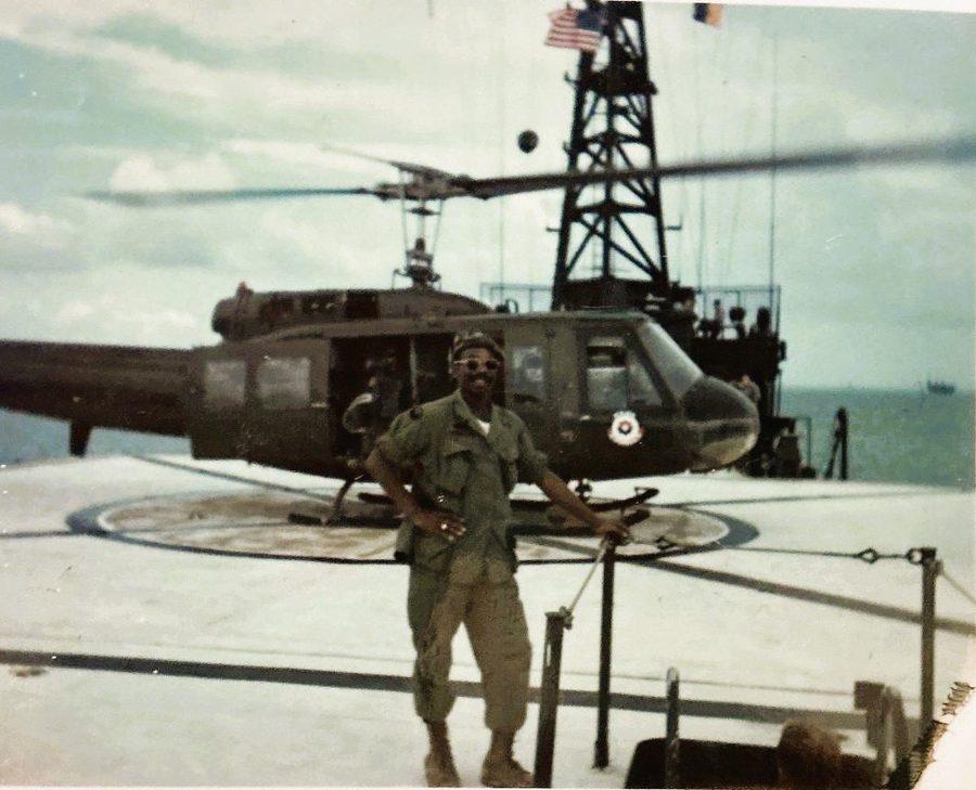 Leon Collier in fatigues and sunglasses in front of a helicopter on a flight deck.