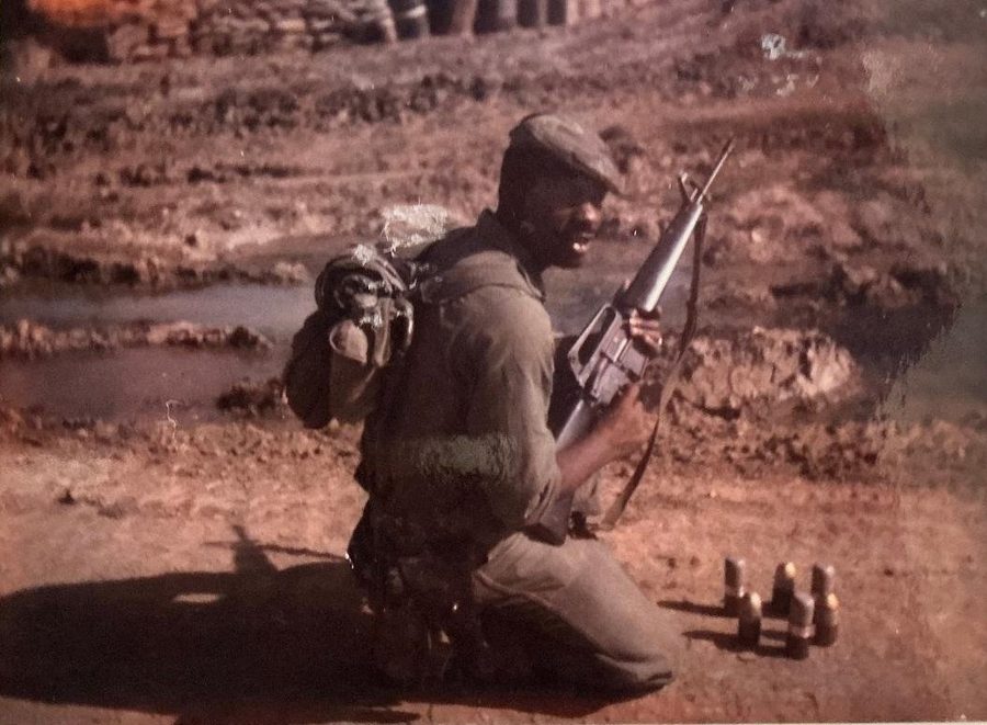 Leon Collier kneeling in the field in fatigues while holding his rifle.